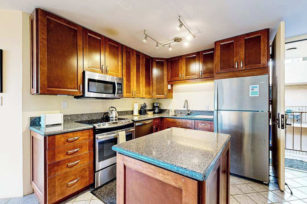 Una cocina con armarios de madera, microondas, estufa, refrigerador y encimera de granito.