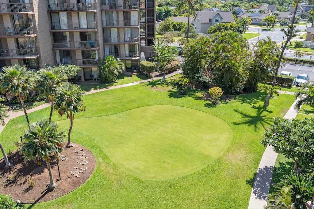 A well-maintained lawn with palm trees, a circular garden bed, and a multi-story building with balconies.