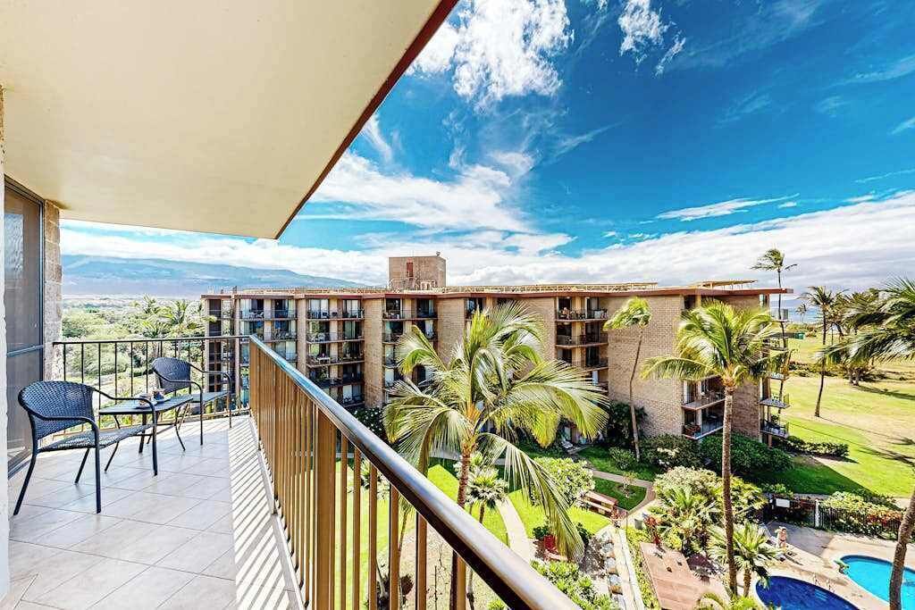 A balcony with chairs, a pool, and a view of a building with multiple floors and balconies.