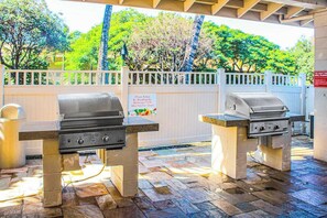 Eine Außenpatio mit zwei Grillstationen, einem weißen Zaun und Bäumen im Hintergrund.