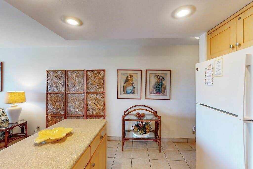 A kitchen with a countertop, a refrigerator, wooden cabinets, and wall-mounted artwork.