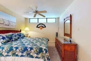 Een slaapkamer met een bed, een dressoir, een plafondventilator, een ventilator aan de muur, een raam en een schilderij.