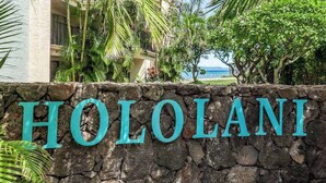 Een stenen muur met de tekst 'HOLOLANI' in turquoise letters.