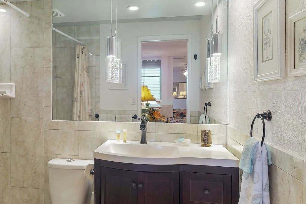 A bathroom with a large mirror, a sink, a toilet, and a towel rack.