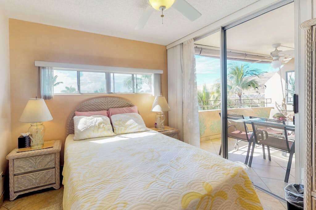 A bedroom with a bed, bedside lamps, a window, and a balcony with outdoor furniture.