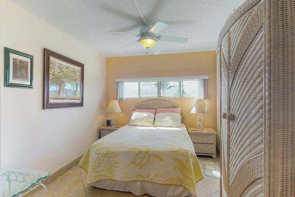 A bedroom with a bed, two bedside tables, a ceiling fan, a window, and a wicker door.