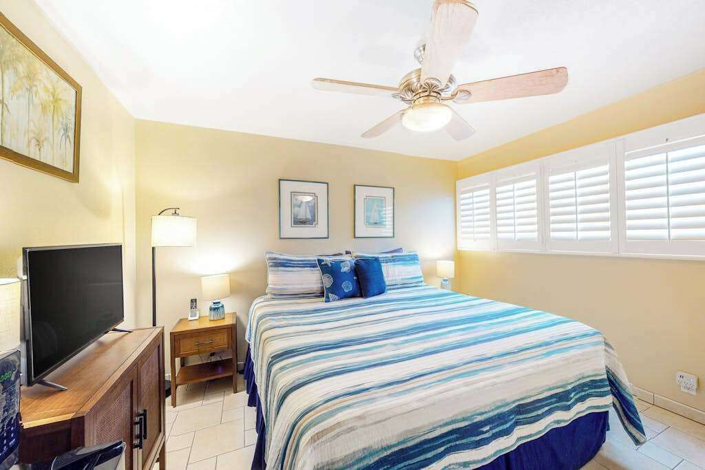 Une chambre à coucher avec un lit, un ventilateur de plafond, une télévision et un bureau.