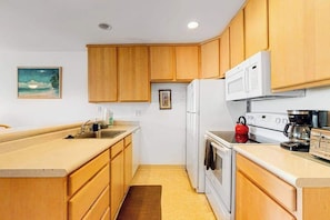 A compact kitchen with wooden cabinets, a white refrigerator, a stove, and a microwave. - *New* Fall $pecial Garden-View Kihei Condo for Four Near Kamaole III (Kihei)
