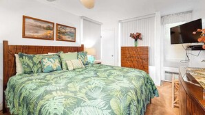 Un dormitorio con cama, ventilador de techo, televisión y obras de arte en la pared.