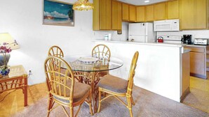 Cocina compacta con armarios de madera, una mesa de comedor de vidrio, sillas de mimbre y una pequeña isla.