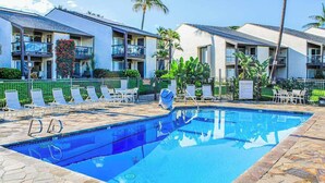 Ein Swimmingpool mit Liegestühlen, einer Steinputz-Terrasse und einem Gebäude mit Balkonen.