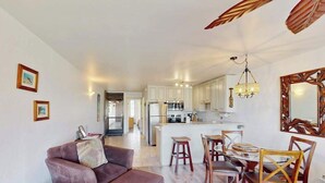 Ein modernes Wohnzimmer mit einer Couch, einem Esstisch mit Stühlen, einer Küche im Hintergrund und einem großen Spiegel an der Wand.