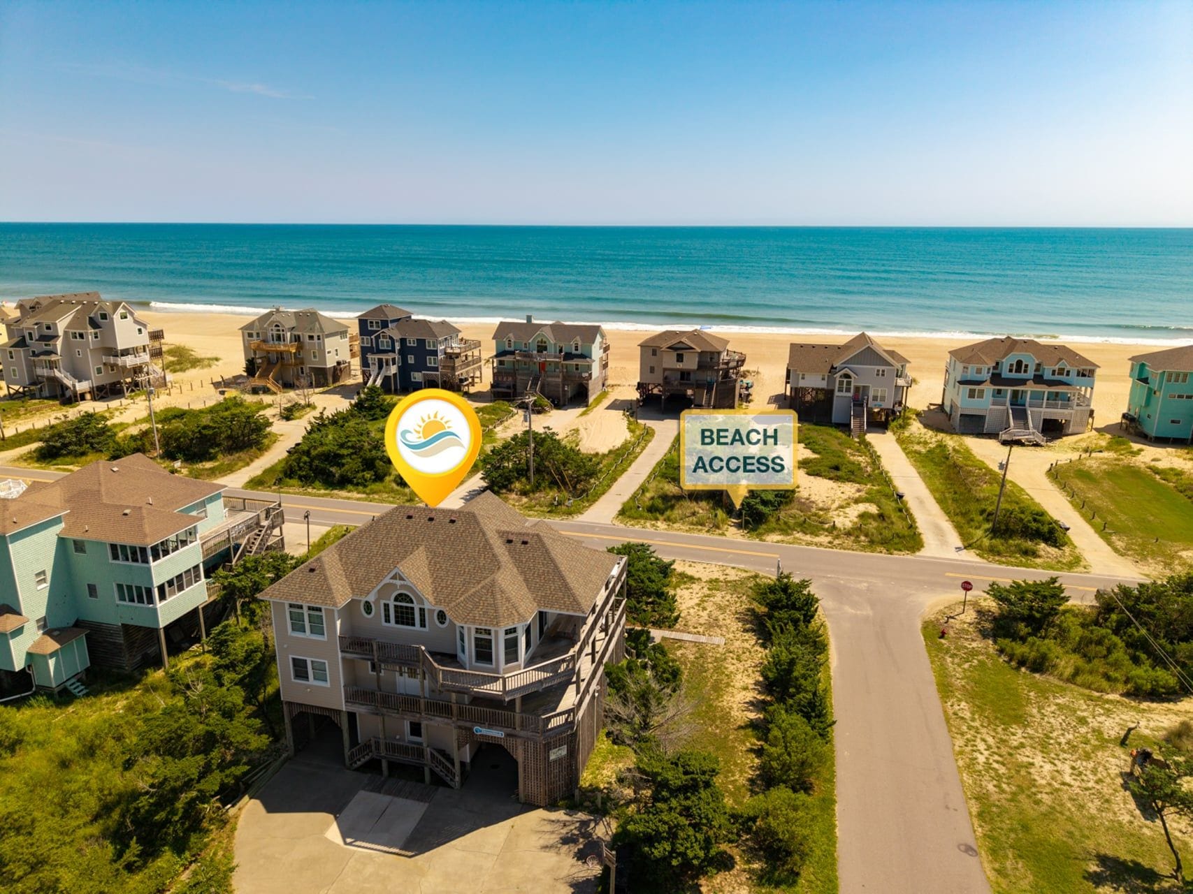 Zona residencial costera con casas, un letrero de acceso a la playa y una carretera que conduce a ella.