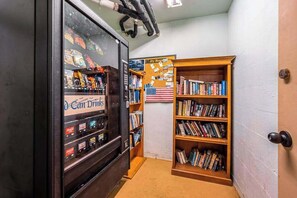 Ein Verkaufsautomat mit Snacks, ein kleines Bücherregal mit Büchern und eine amerikanische Flagge an der Wand.