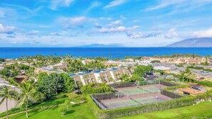 Un resort con varias construcciones, una cancha de tenis y vista al océano.