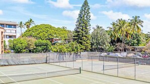 Ein Tennisplatz im Freien, umzäunt, mit Bäumen und Gebäuden im Hintergrund.