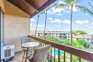 A balcony with wicker chairs, a table, and an air conditioning unit. - New Fall Deal Top-Floor Ocean Views Across from Charley Young Beach (Kihei)