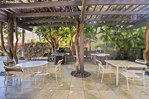 Ein Außenbereich mit einer Terrasse, zwei Grillanlagen, runden Tischen und Stühlen.