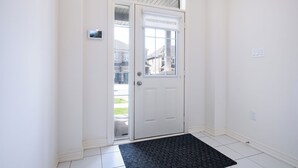 Una puerta blanca con un panel de vidrio, un felpudo negro y un suelo de baldosas blancas.
