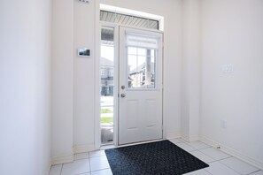Eine weiße Tür mit Glasfenster, eine schwarze Fußmatte und ein weiß gefliester Boden.
