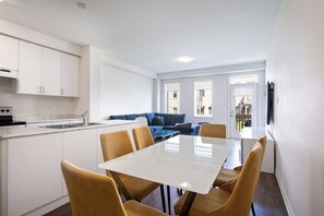 A modern kitchen with white cabinets, a stove, and a sink. There is a dining area with a white table and four chairs. A blue sofa is visible in the background. - Lovely 3-bedroom apartment with AC in charming Cambridge (Cambridge)