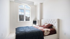 Un dormitorio con cama, ventana, mesita de noche y una silla.