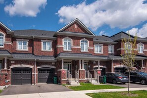 A row of brick townhouses with attached garages, a clear sky, and a small tree in the foreground. - Lovely 3-bedroom apartment with AC in charming Cambridge (Cambridge)