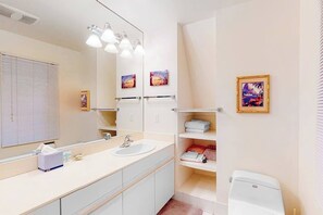 Un baño moderno con un espejo grande, un lavamanos, un inodoro y estantes con toallas.