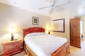 Un dormitorio con una cama, dos mesitas de noche con lámparas, un armario de madera y un ventilador de techo.