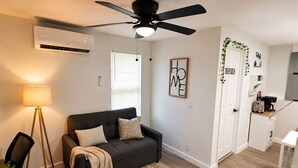 Uma sala de estar moderna com um sofá, uma mesa pequena, um ventilador de teto e uma área de cozinha compacta.