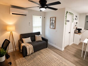 Ein modernes Wohnzimmer mit einer Couch, einem kleinen Tisch, einem Deckenventilator und einer Küchenzeile.