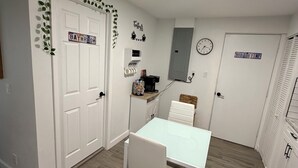 Quarto pequeno e limpo com uma mesa branca e cadeiras, um relógio e um aviso que diz 'HOT TUB TIME'.