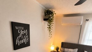Quarto com cama, mesa de cabeceira, abajur e ar condicionado na parede.