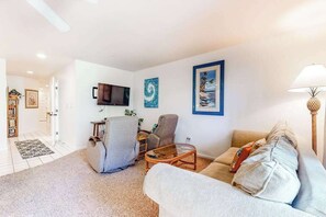 Ein Wohnzimmer mit Sofa, Sessel und Couchtisch, einem Flachbildfernseher und gerahmten Kunstwerken an der Wand.