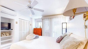 Ein Schlafzimmer mit Bett, Deckenventilator, Fernseher und einem Fenster mit Jalousien.
