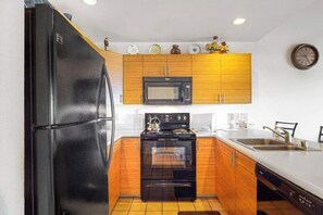 Eine kompakte Küche mit einem schwarzen Kühlschrank, Holzschränken, einer Mikrowelle, einem Backofen und einem Geschirrspüler.