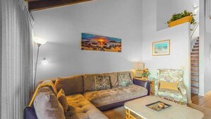 Ein Wohnzimmer mit Ecksofa, einem kleinen Tisch, einem Sessel, einer Lampe und einem Bild an der Wand.