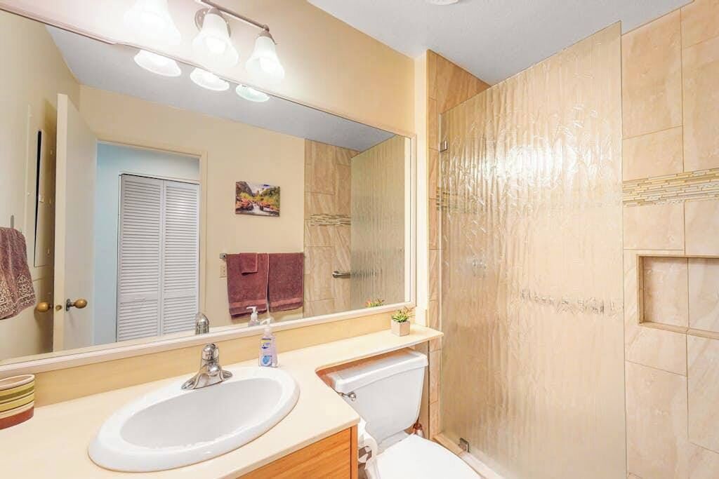 Un baño con un espejo grande, dos lavamanos, un inodoro y una ducha.