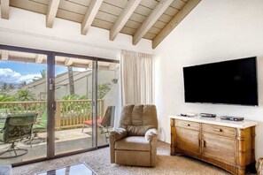 A living room with a sliding glass door leading to a balcony, a flat-screen TV mounted on the wall, and a wooden cabinet. - *New* Fall Deal Two-Level Kihei 2BR with Loft and Three Lanais (Kihei)