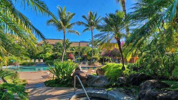 Un área de piscina con jacuzzi, palmeras y un edificio al fondo.