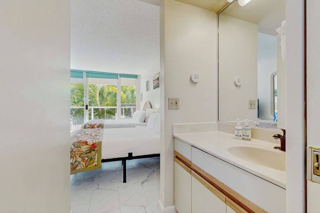Une chambre à coucher avec un lit, une grande fenêtre et une salle de bain équipée d’un lavabo et d’un miroir.