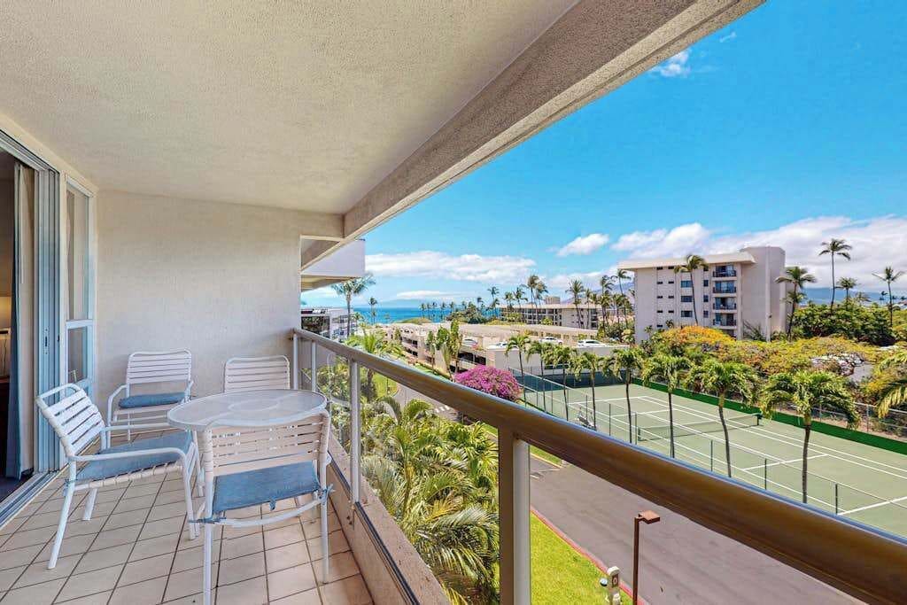 A balcony with a view of a tennis court, palm trees, and a building in the background.