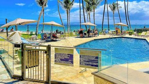 A poolside area with palm trees, lounge chairs, and a clear view of the ocean. - NEW Ocean-View Keawakapu Beach Suite for Four (Kihei)