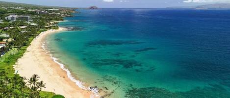 A coastal view with a beach, clear waters, and a distant mountain.
