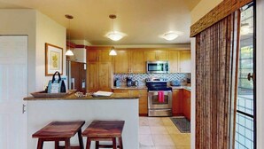 Une cuisine avec des meubles en bois, un four à micro-ondes et une cuisinière. On y trouve deux tabourets en bois et un petit îlot central avec un plan de travail.