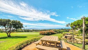 Une table de pique-nique placée dans un cadre extérieur ensoleillé, avec vue sur un terrain de golf et sur des montagnes lointaines.
