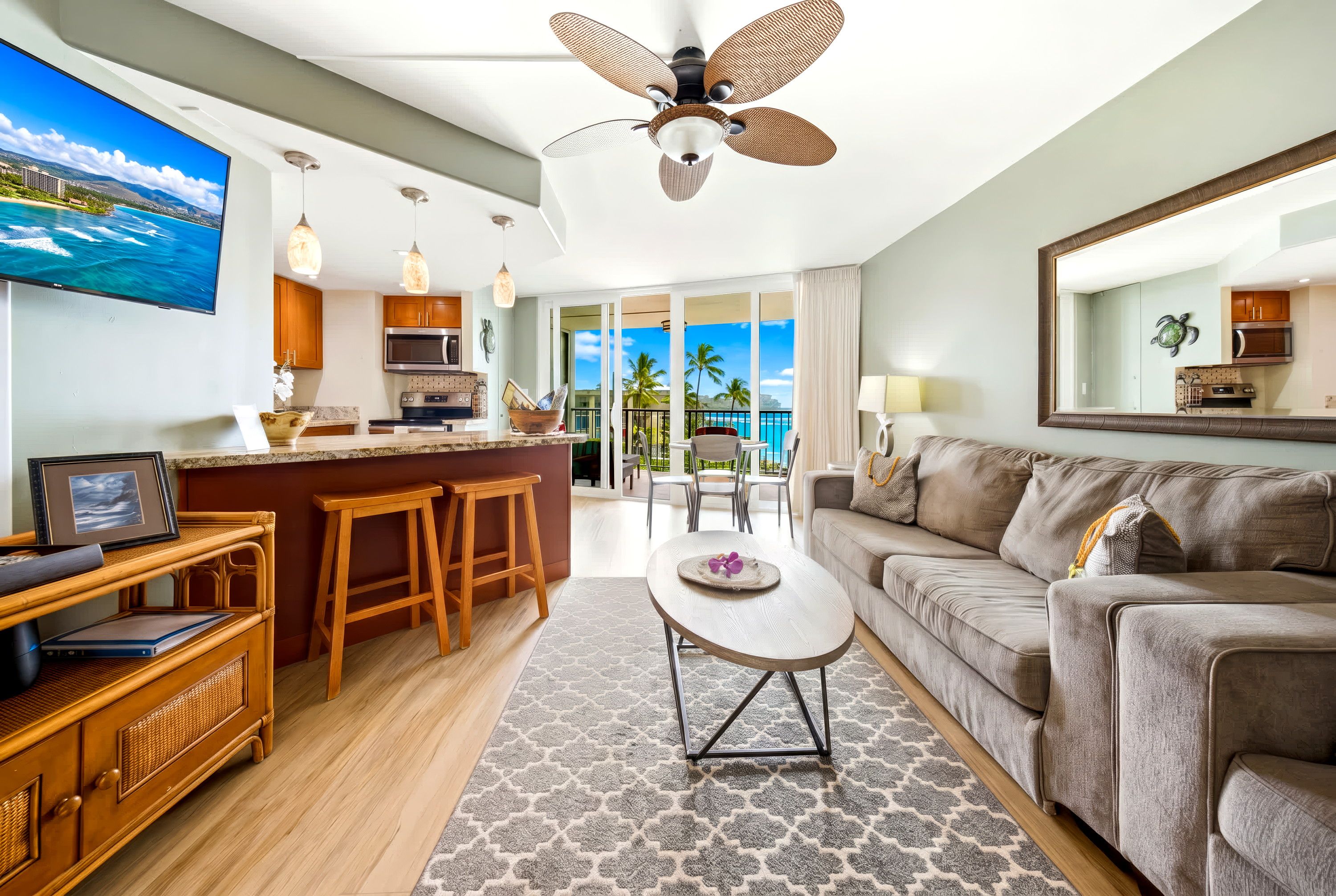 A modern hotel room with a kitchen, dining area, and a balcony with a view of the ocean.