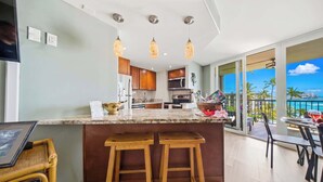A modern kitchen with a bar area, large windows, and a view of the ocean. - *New* Fall Special Oceanfront Honokōwai Retreat with a Spacious Lanai (Lahaina)
