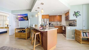 A modern kitchen with a central island, wooden bar stools, and a large island with a built-in sink. - *New* Fall Special Oceanfront Honokōwai Retreat with a Spacious Lanai (Lahaina)