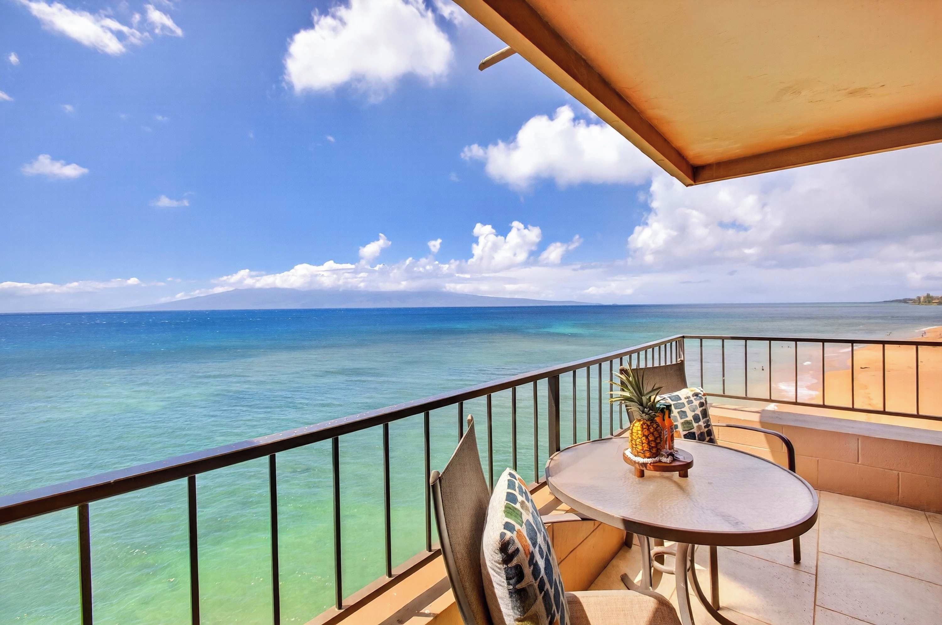 A balcony with a view of the ocean, a table with chairs, and a pineapple on the table.